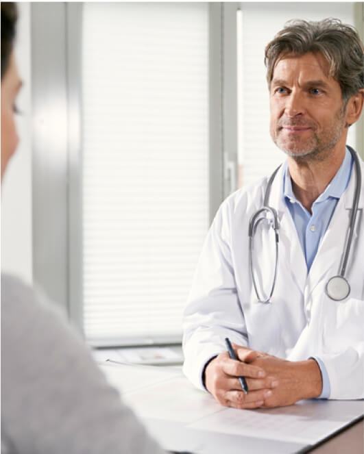 A cardiologist, wearing a white coat and stethoscope, sits at a desk, attentively listening to a patient not fully visible in the foreground. His independent practice allows him to focus on personalized care while also dedicating time for business planning.