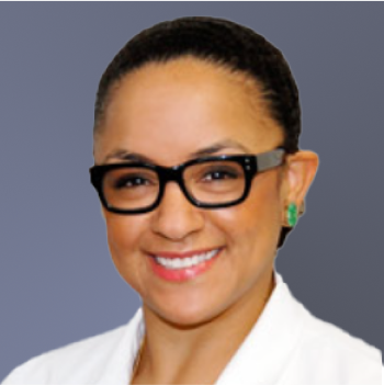 A person with black glasses, short hair, and a white lab coat smiles against a grey gradient background.