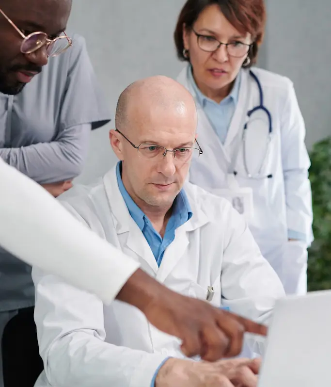 Three doctors review information on a laptop, with one doctor pointing at the screen.