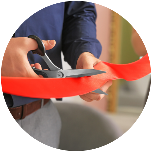 A person in a blue shirt uses scissors to cut a red ribbon, likely during a ceremonial event or grand opening.